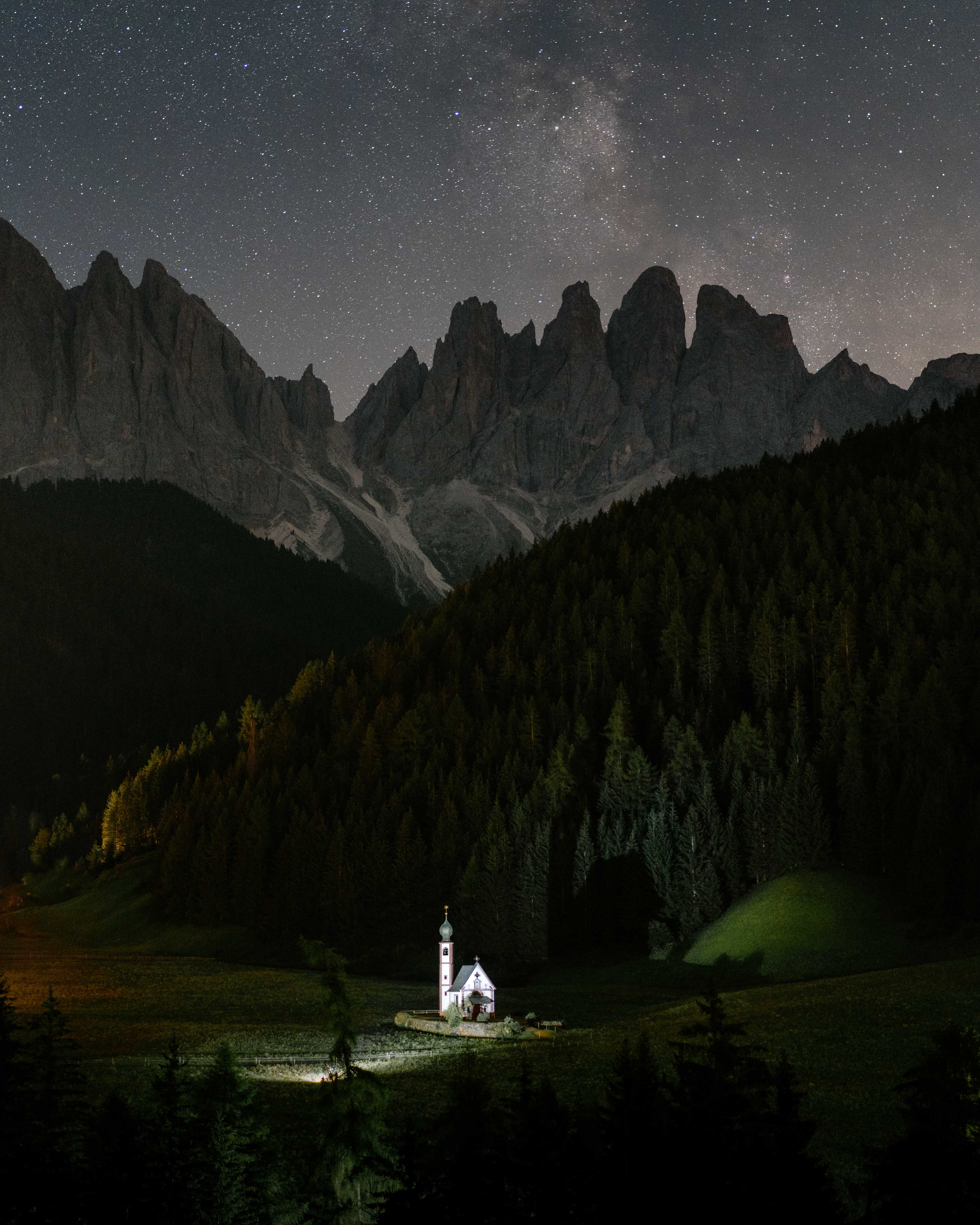 A small church in front of a rocky mountain range under the stars